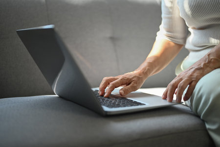 Happy middle age woman in casual clothes using laptop on couch in cozy home.の写真素材