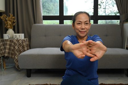 Happy senior woman stretching her arms before meditation and wellness workout at homeの写真素材