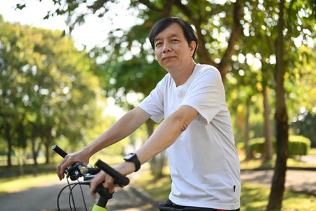 Portrait of happy retired man riding electric bicycle in public park on sunny day. Healthy lifestyle conceptの写真素材