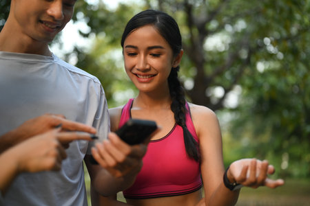 Smiling male and females athletic taking a break and looking fitness app on mobile phoneの写真素材