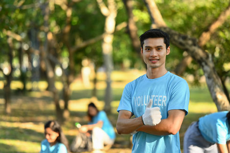 Positive male volunteer in blue uniform smiling at camera while standing outdoor. Charity and community service concept.の写真素材
