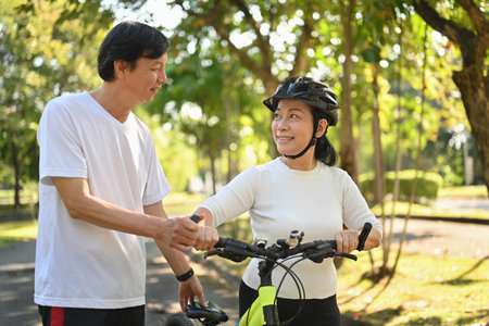 Beautiful active middle age couple with bicycle walking through park on sunny summer dayの写真素材