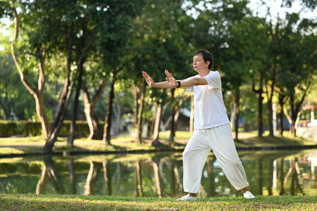 Full length senior man practicing Tai Chi outdoor near lake at sunset in summer parkの写真素材