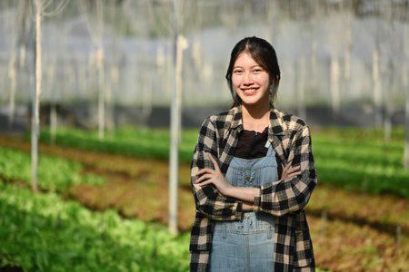 Portrait of cheerful female farmer standing with crossed arms at greenhouse of organic vegetables.の写真素材