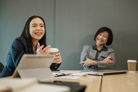 Cheerful Asian female manager talking to colleagues during break at meeting roomの写真素材