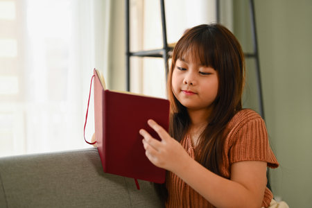 Happy Asian girl n casual clothes reading a book on couch at homeの写真素材