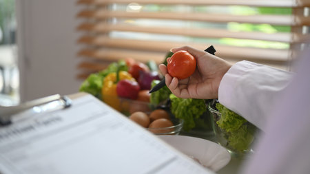 Nutritionist hand holding tomato and prescribing recipe at desk. Healthcare and diet conceptの写真素材