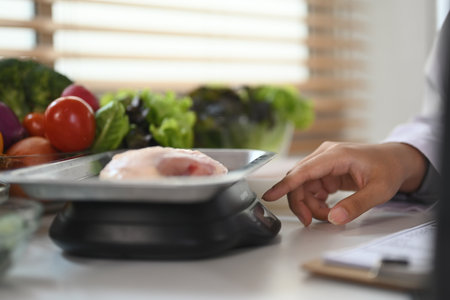 Nutritionist weighing raw chicken breast on a scale during consultation in hospitalの写真素材