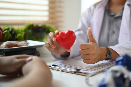 Nutritionist holding red heart shape during conversation with patient at clinic. Right nutrition and...