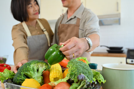 Happy middle age couple preparing healthy salad in the kitchen with organic vegetableの写真素材