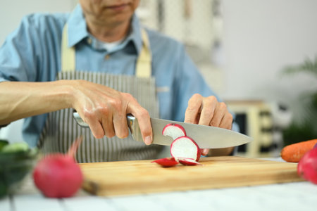 Closeup senior man cutting fresh radish on board while preparing healthy lunch in home kitchenの写真素材