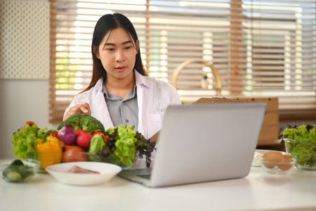 Female nutritionist in white coat calling patient and giving online consultation on laptop computer.の写真素材