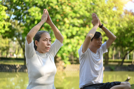 Older active couple doing breathing exercise in the summer park. Healthcare and meditation conceptの写真素材