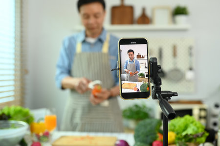Middle age man recording video with healthy recipe of green smoothie on smartphoneの写真素材