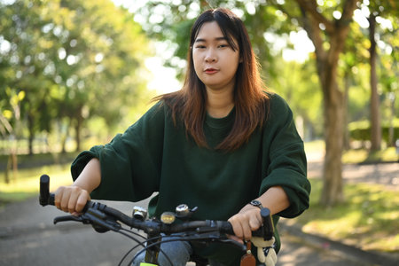 Happy young Asian woman riding a bicycle through the city park. Active urban lifestyle conceptの写真素材