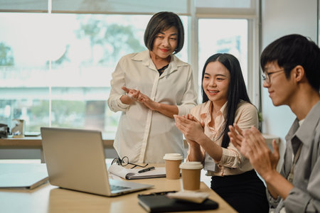Corporate team looking at laptop screen surprised by good online news and clapping hands in co working spaceの写真素材