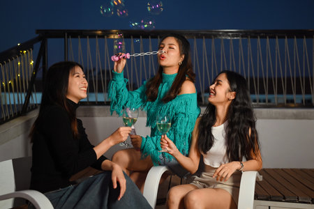 Young friends gathered together having fun toasting champagne and blowing soap bubbles at the rooftop night partyの写真素材
