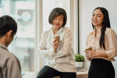 Friendly senior businesswoman taking coffee break after conference with younger colleaguesの写真素材