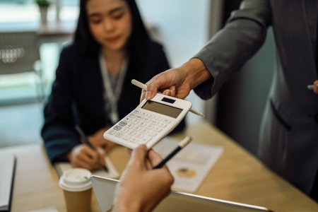 Female team leader showing finances or calculations on a calculator to colleagues in a meetingの写真素材