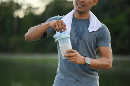 Image of athletic sportsman drinking protein shake after morning cardio workout in the park.の写真素材