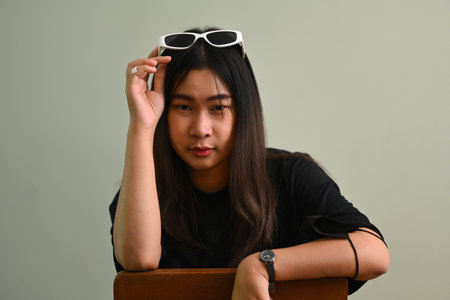Portrait of pretty young woman in black t-shirt holding sunglasses and looking at camera.