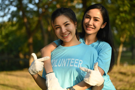 Two cheerful women pointing finger on volunteer title text on t-shirt while standing outdoor.の写真素材