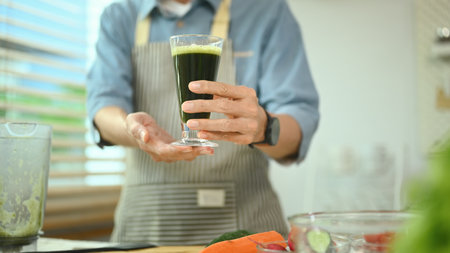 Healthy senior man holding a glass of green vegetable smoothie near ingredients in kitchen.の写真素材
