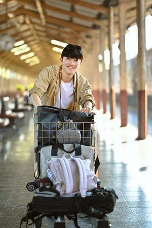 Attractive young man pushing a luggage cart walking on the corridor at railway station.の写真素材