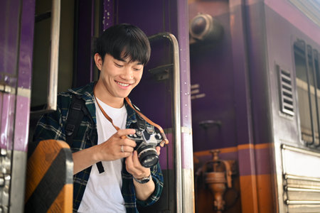 Happy male tourist with backpack checking photo on camera at the railway station.の写真素材