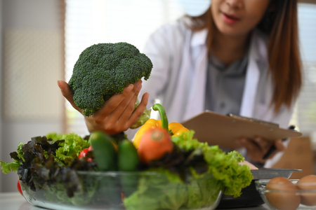 Nutritionist in white coat working in her clinic, showing healthy vegetables and fruits.の写真素材