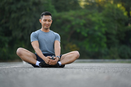 Full length of handsome sporty man stretching legs while exercising outdoors.の写真素材