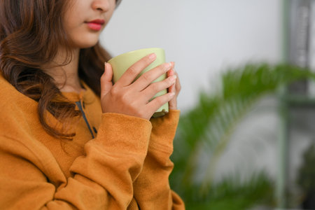 Cropped shot young woman in yellow sweater holding cup of coffee. People, relaxation and lifestyle conceptの写真素材