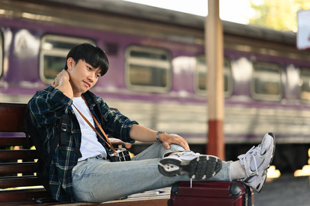 Asian male traveller sitting on bench waiting for train at railway station . Travel and lifestyle concept.の写真素材