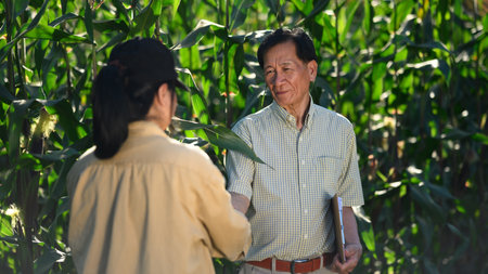 Smiling senior male farmer and female agronomist shaking hands at the cornfield.