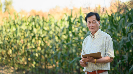 Portrait of successful senior male farmer standing in corn field. Agribusiness concept.