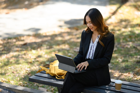 Charming businesswoman sitting on the bench in the city park and using digital tablet.の写真素材