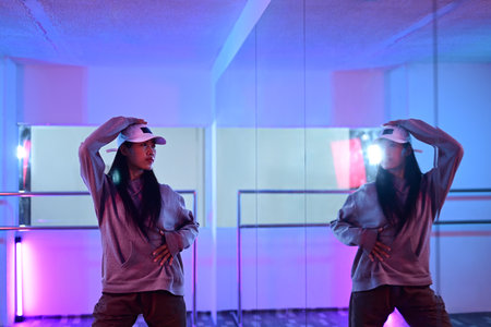 Young woman dancing hip hop style in front of mirror at studio with neon light.