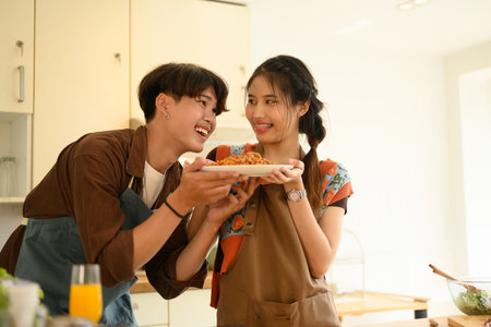 Happy Asian couple holding plate of spaghetti, cooking in kitchen together on weekend.