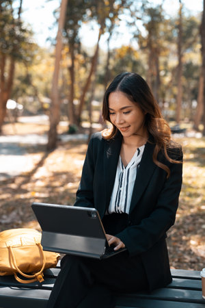 Portrait of attractive businesswoman sitting on a park bench and using digital tablet.の写真素材