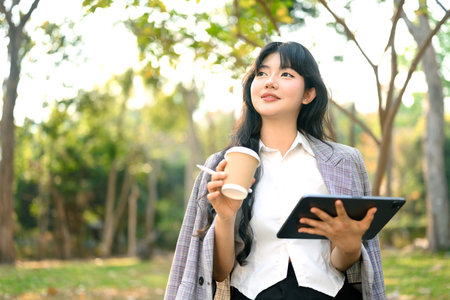 Portrait smiling female entrepreneur holding a takeaway paper cup of coffee and looking away at park.の写真素材