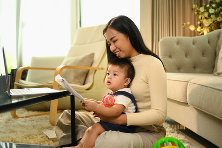 Beautiful young mother working remotely on laptop while taking care of her baby during maternity leave.の写真素材