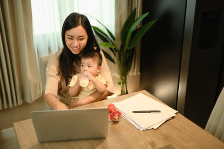 Loving young mother working remotely on laptop while taking care of her baby.の写真素材