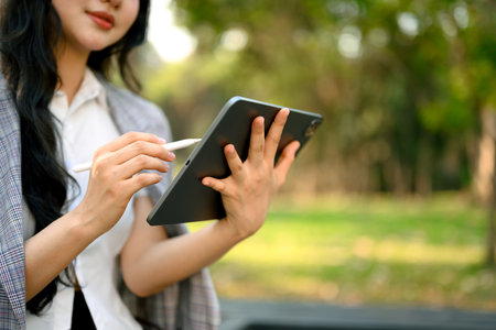 Cropped shot young female worker using digital tablet while relaxing in the public park.