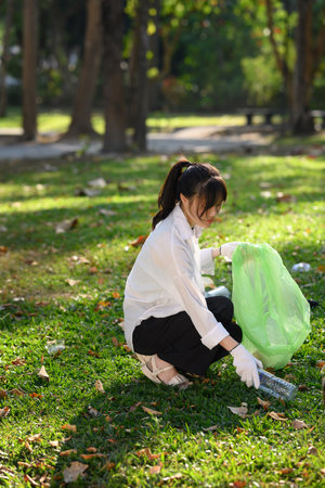 Portrait of young woman picking up litter in the park on a sunny bright day. Environmental protection concept.の写真素材