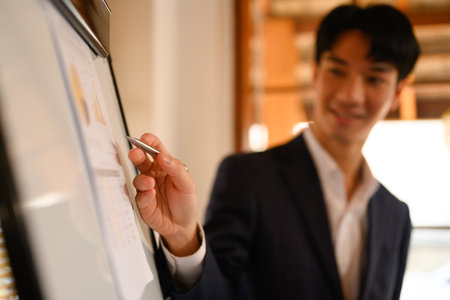 Young businessman giving a presentation about financial research on whiteboard during meeting.の写真素材