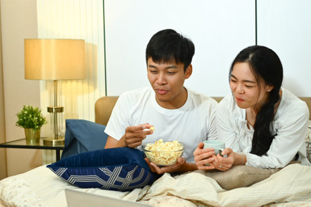 Happy marriage couple watching TV and eating popcorn on couch at home.の写真素材
