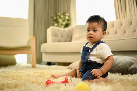 Cute little baby boy sitting on fluffy carpet on and playing with toys in living room.の写真素材