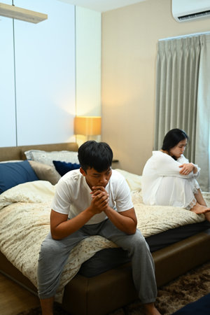 Sad thoughtful man sitting on bed after arguing with girlfriend. Conflict and relationship concept.の写真素材