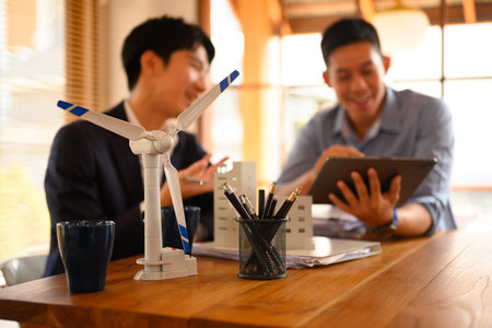 A wind turbine model on table with two businessman working in background. Alternative energy concept.の写真素材