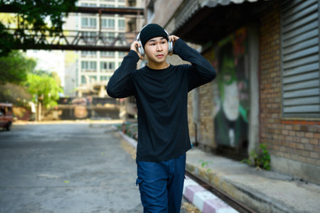 Stylish young Asian man listening to music in headphones and walking down the street in the urban city.の写真素材